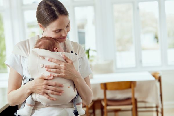 Frau trägt ein Baby in einer Tragehilfe vor der Brust und hält es in den Armen.